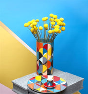 Vista Alegre | Futurismo Charger Plate with vibrant geometric patterns, displayed with matching vase and candle-holder, set atop a concrete plinth, embodying modern, Pop-Art style.
