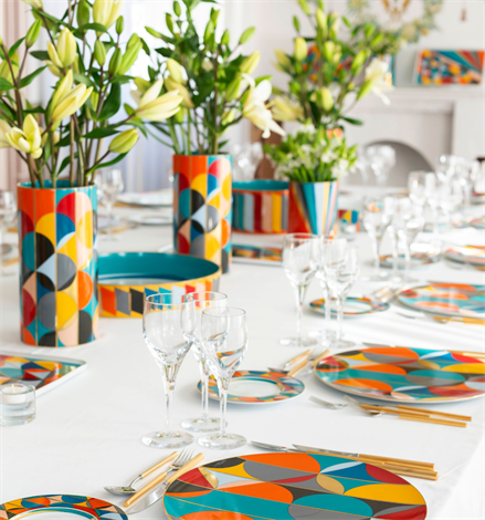Vista Alegre | Futurismo Bread And Butter Plate on a set table with geometric patterned dinnerware, gold-tone flatware, and floral runner of lilies.