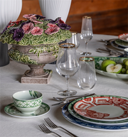 Vista Alegre | The Meaning Charger Plate displayed in an elegant table setting with floral centerpiece, gold-rimmed glassware, and coordinated dinnerware.