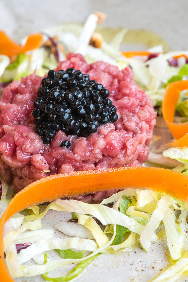 TartufLanghe Truffle Perlage atop steak tartare, accented with black caviar, carrot ribbons, and lettuce, exemplifying modern gastronomy for gourmet culinary creations.