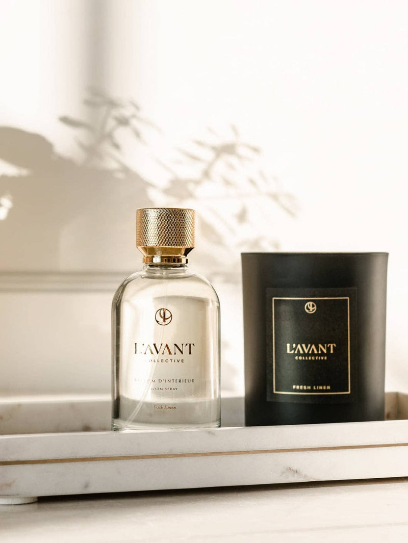 L'AVANT Collective - Fresh Linen Room Spray 100 ml alongside a candle on a marble shelf, showcasing luxury and elegance in home fragrance.