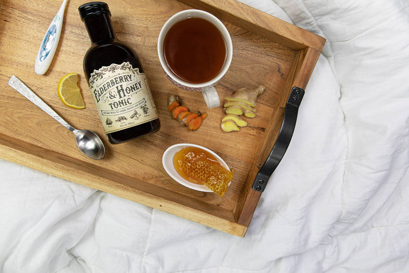 Roots And Leaves - Elderberry & Honey Tonic, 16 oz bottle on a tray with honey and lemon, highlighting its herbal immune support formulation.