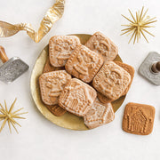 Nordic Ware | Gingerbread cookie stamps displayed with cookies and festive decorations, showcasing intricate holiday designs for creating themed treats.