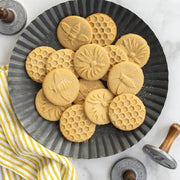 Nordic Ware | Honey Bees Cookie Stamps on a plate of intricately designed cookies featuring bee, flower, and honeycomb patterns, showcasing the detailed results of these stamps.