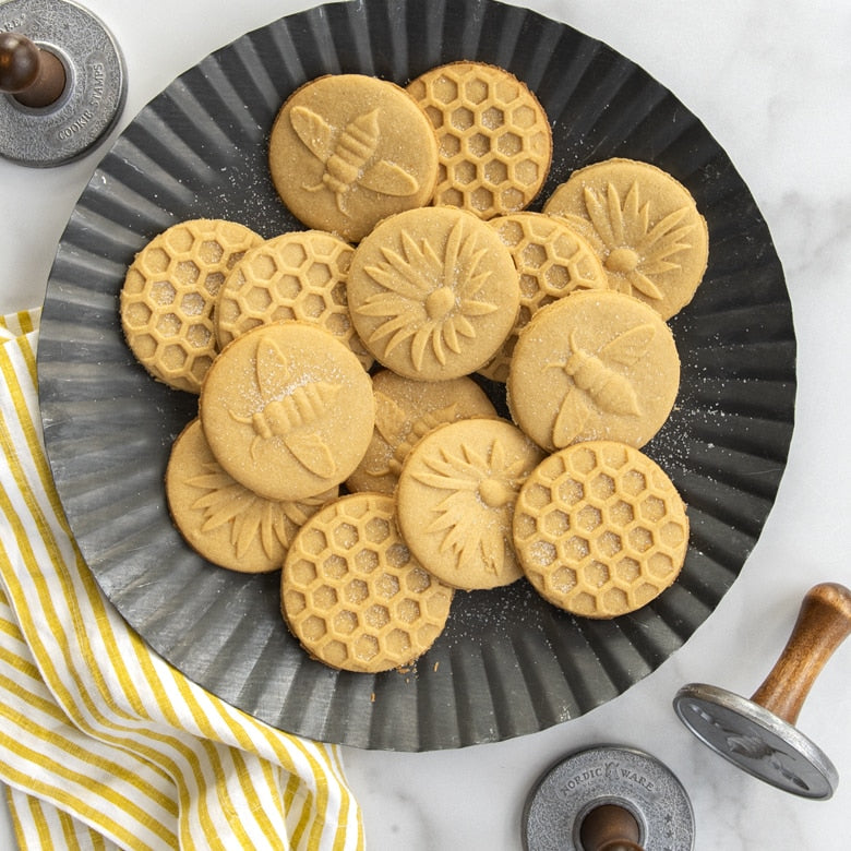 Nordic Ware | Honey Bees Cookie Stamps on a plate of intricately designed cookies featuring bee, flower, and honeycomb patterns, showcasing the detailed results of these stamps.
