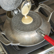 Nordic Ware | Norwegian Krumkake and Pizzelle Iron set with spoon pouring liquid onto the pan for traditional cookie making, including press, cooking base, and wooden cone.