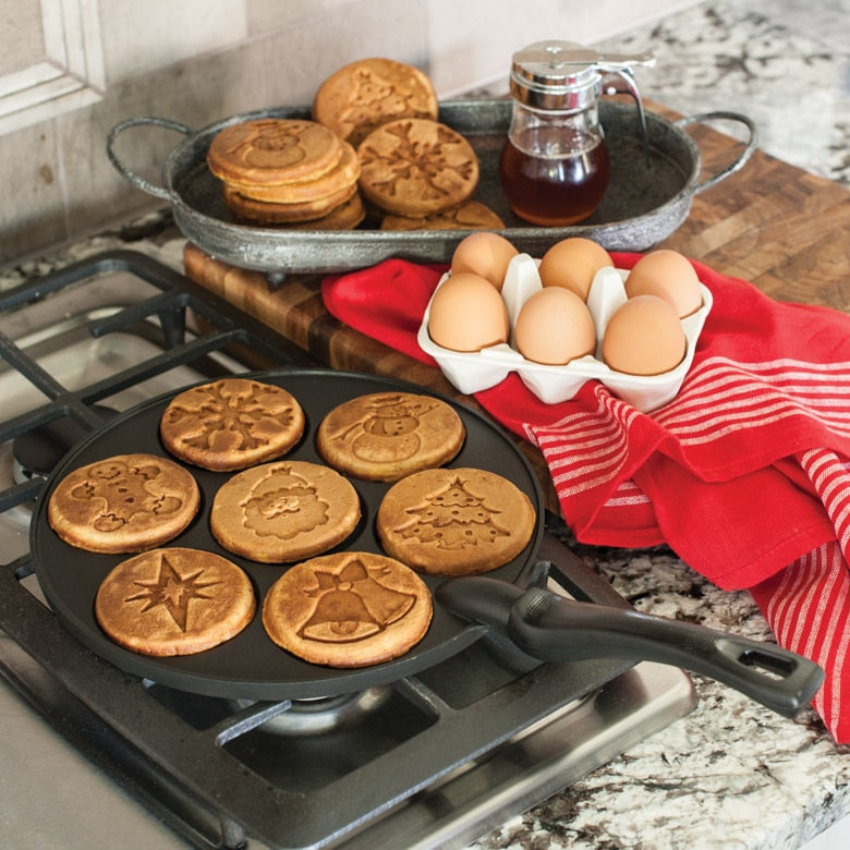 Nordic Ware | Holiday Pancake Pan with festive designs for making seven 3-inch pancakes, shown with pancakes on a pan next to eggs and cookies.