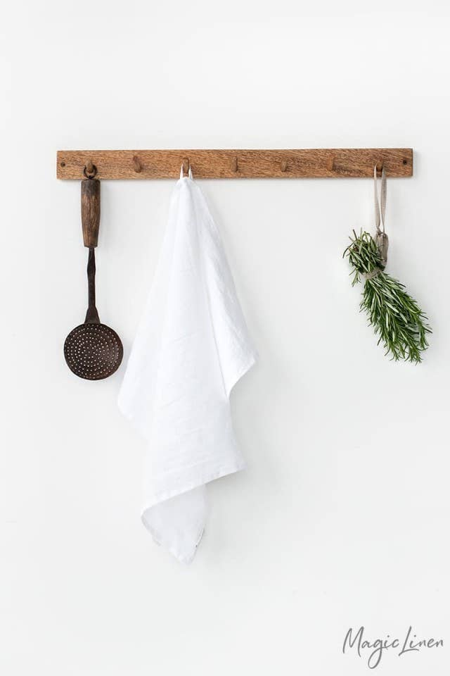 Linen tea towel hanging on a wooden rack with herbs and a wooden spoon, showcasing its absorbent, durable quality, ideal for kitchen use.