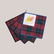 Atelier Saucier | Jubilee Plaid Cocktail Napkins, Set of 4. Features red-and-green tartan, each with a unique colored piped edge, perfect for holiday entertaining.