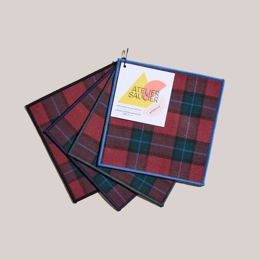 Atelier Saucier | Jubilee Plaid Cocktail Napkins, Set of 4. Features red-and-green tartan, each with a unique colored piped edge, perfect for holiday entertaining.