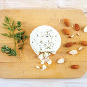 Cypress Grove | Herbs de Humboldt Goat Cheese on a wooden board, showcasing a round, herb-coated cheese with a creamy white interior.