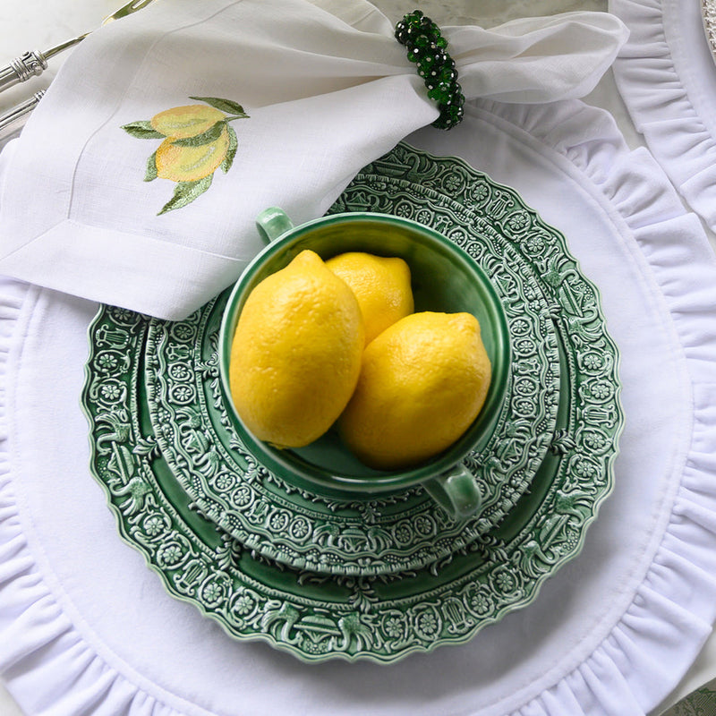 Arte Italica & Crown Linen Designs Renaissance Dinner Plate in green, featuring ornate patterns, topped with lemons and a matching bowl, on a white ruffled placemat.