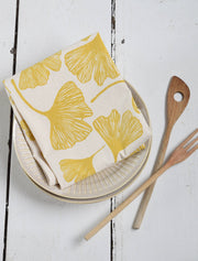 Hearth and Harrow - Ginkgo Leaf Tea Towel - Organic Cotton, displayed folded on ceramic plates with wooden utensils, showcasing its eco-friendly design and oversized 30 x 30 size.