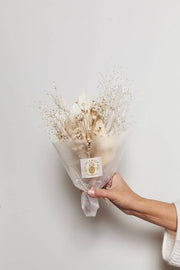 Idlewild Floral Co. - Snow Dried Flower Bouquet held in hand, featuring neutral-toned dried flowers and grasses, wrapped in translucent paper with label, ideal for home decor or gifting.
