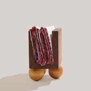 Atelier Saucier | Les Trois Wooden Napkin Holder featuring a dark walnut box on birch wood legs, with colorful textiles draped over its U-shaped opening.