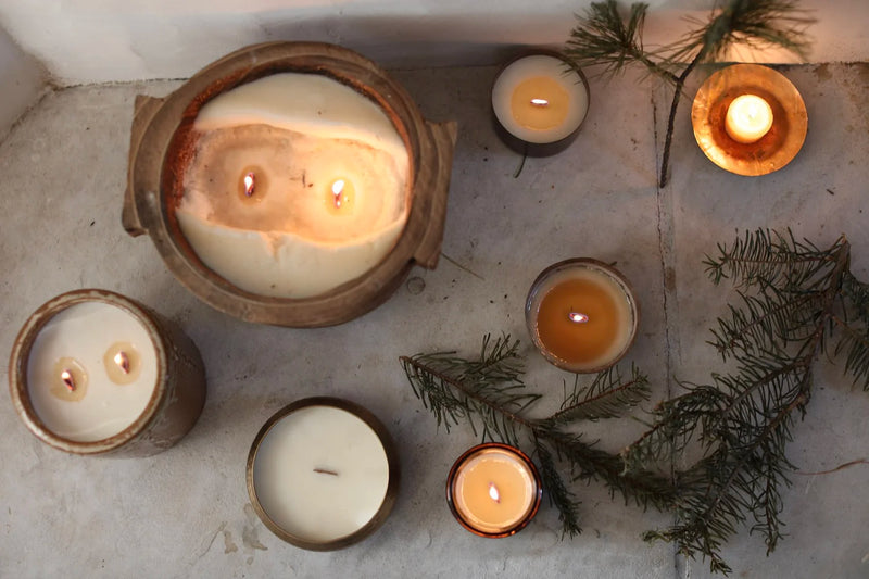 Overhead view of Among the Flowers | Essential Oil + Soy Wax Candle Wilder, in rustic holders with evergreen sprigs, creating a cozy, informal ambiance on a stone surface.
