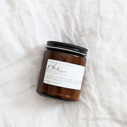 Among the Flowers | Essential Oil Candle, Through the Woods in a small amber-glass jar with a black lid, featuring a white label, handcrafted in California.