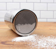 Shaker - Fine Mesh on a table, featuring a compact design with a mesh insert and plastic top, ideal for spices or powdered sugar.