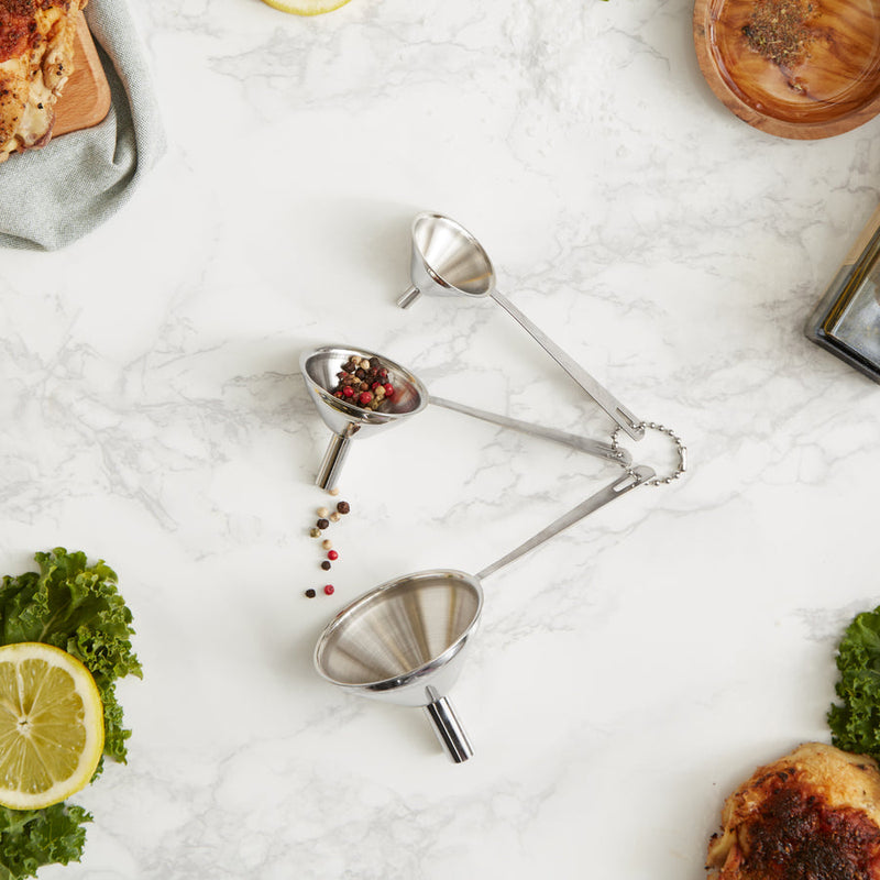 Set of three mini stainless steel funnels on a marble surface, ideal for precise kitchen tasks. Perfect for transferring liquids and spices.