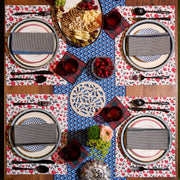 Overhead view of a wooden dining table set with Atelier Saucier Jubilee Plaid Cocktail Napkins, featuring a coordinated cheese-and-fruit spread and matching glassware.