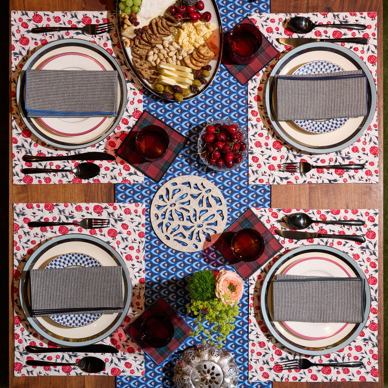 Overhead view of a wooden dining table set with Atelier Saucier Jubilee Plaid Cocktail Napkins, featuring a coordinated cheese-and-fruit spread and matching glassware.