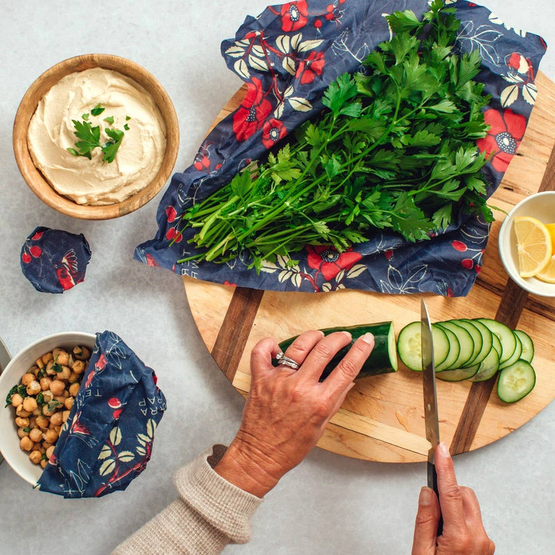 Hands preparing veggies on a board using Bee's Wrap - Assorted 3 Pack - Botanical to cover bowls, emphasizing sustainable, reusable food storage in a kitchen setting.