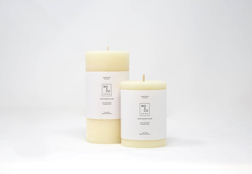 Mo&Co Home - 100% Beeswax Pillar Candles | Natural White: 3x4 Inch. Two hand-poured white candles with labels, showcasing sustainable craftsmanship.