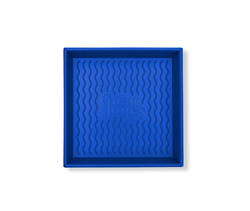 Great Jones | Square One - Blueberry: A 9x9-inch blue baking pan with a wavy, corrugated bottom for easy release, featuring nonstick, nontoxic coating.