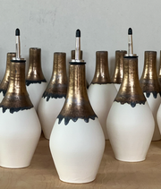 Jessica Wertz Ceramics - Gold + White Oil Bottle: Black, a handmade ceramic dispenser with stainless-steel spout, featuring a white matte glaze and metallic bronze drip, on a wooden shelf.