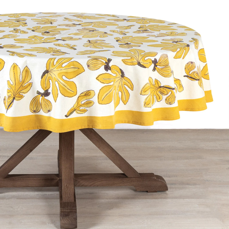Round table featuring the Caravan Home 71 x 71 Fig Citrine Tablecloth with a yellow and white leaf pattern, ideal for kitchen decor.