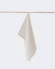 Linen tea towel hanging from a wooden stick, showcasing its texture and loop for easy hanging, ideal for kitchen use due to its absorbency and durability.