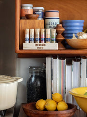 Jacobsen Salt Co. - Infused Sea Salt Gift Set with Wooden Stand displayed on a kitchen shelf with spices, cookware, and cookbooks at Athens Cooks.