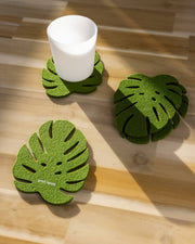 Graf Lantz - Merino Wool Monstera Coaster Set on a table, featuring a glass cup and coasters, adding organic glamour to dining settings.