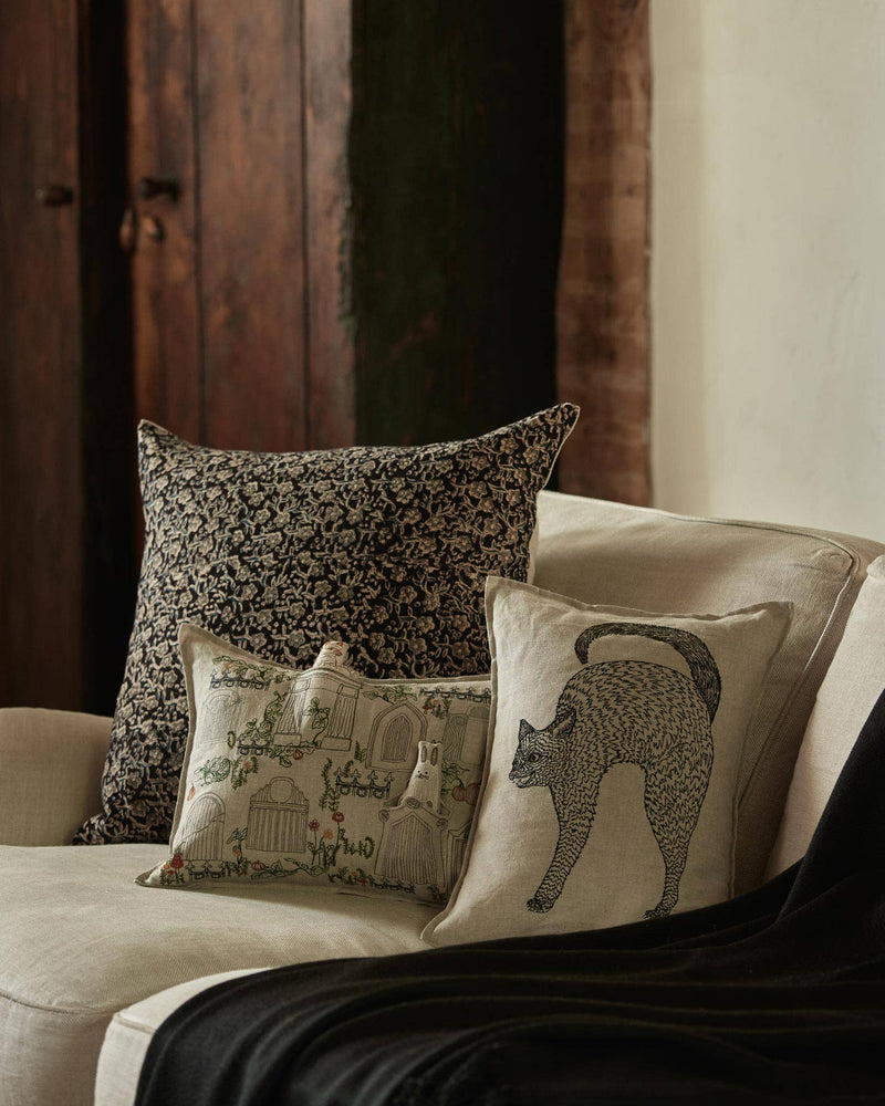Coral & Tusk - Scaredy Black Cat Pillow: An embroidered cat pillow on an off-white sofa, featuring an arched-back black cat design, perfect for Halloween decor.