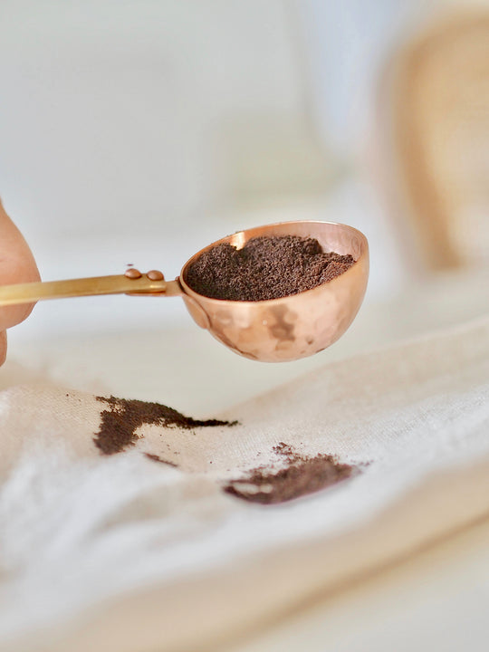 Be Home | Camden Scoop: A handcrafted copper spoon with a rippled texture, held by a person, showcasing its use with ground coffee, reflecting artisan craftsmanship.