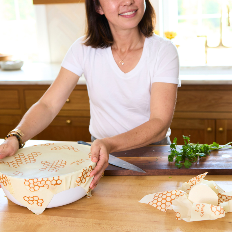 Woman in a kitchen holding Bee's Wrap - Cut-to-Size Roll, showcasing its versatility for eco-friendly food storage solutions.
