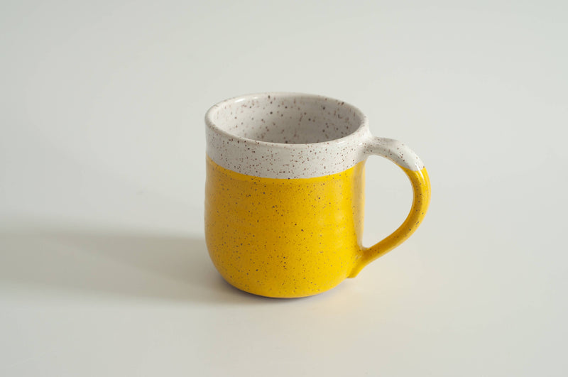 RachaelPots - 12 Oz Original Mug: Sage, a hand-thrown, speckled ceramic mug with a mustard-yellow glaze, featuring a thumb rest, perfect for coffee or tea.