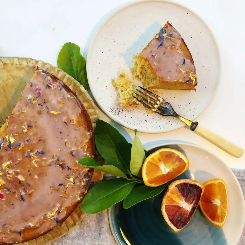 Tabletop spread features a lightly frosted cake with edible flowers, highlighting Hayden Flour Mills - Semolina Flour’s versatility in creating delectable desserts and more.