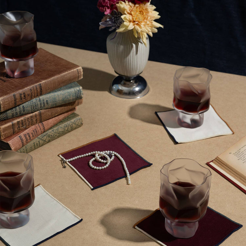 ATELIER SAUCIER - Clubhouse Cocktail Napkins, set of 4, enhance a stylish scene with crumpled-look tumblers and vintage books, embodying comfort and luxury.