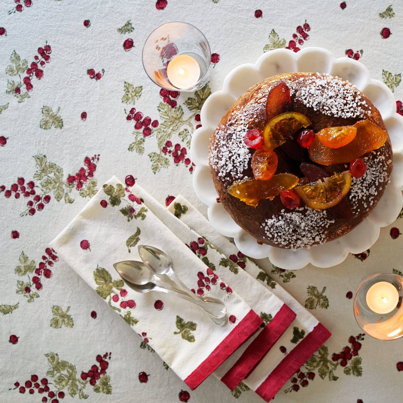 Couleur Nature - Gooseberry Red & Green Tablecloth with festive sugar-dusted cake, candied fruit, and lit candles on a holiday-themed table setting.