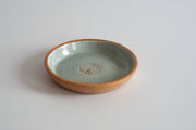 RachaelPots - Garlic Scraper: Coral, a handcrafted ceramic dish with a speckled rim and pale green-blue glaze, designed for transforming garlic into puree.