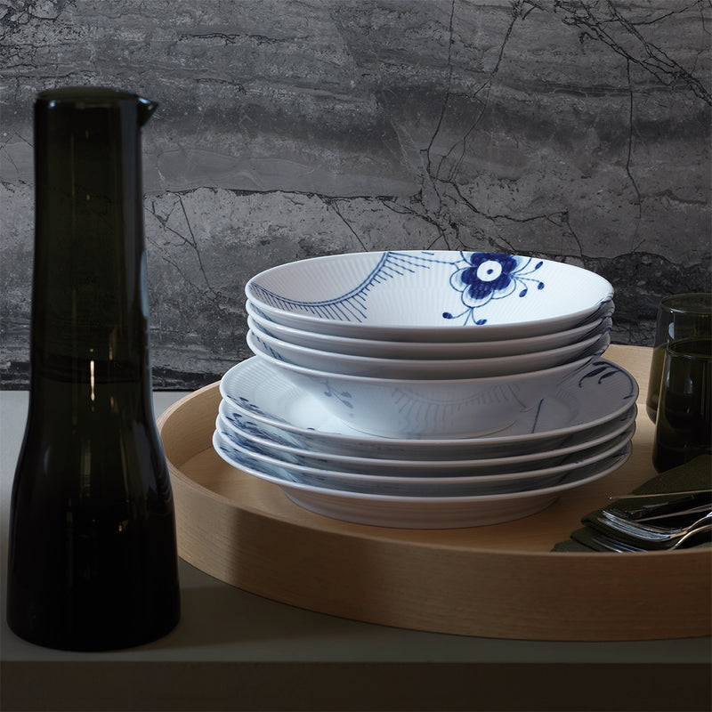 Royal Copenhagen | Blue Mega Deep Plate, 24cm, featuring a blue floral motif, sits atop a wooden tray alongside glassware and cutlery, embodying elegant Danish design.