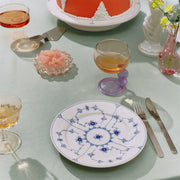 Royal Copenhagen | Blue Fluted Plain Plate, 22cm, featuring hand-painted blue floral motifs, elegantly set with stemmed glasses and a cake on a mint-green tablecloth.