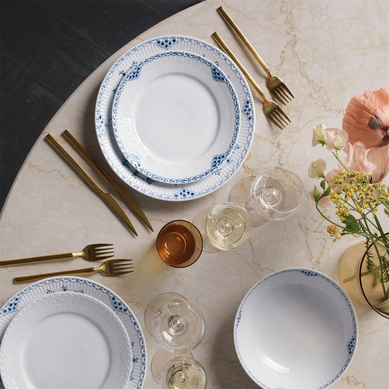 Royal Copenhagen | Blue Fluted Hl Plate, 27cm, elegantly set with gold flatware and wine glasses on marble, surrounded by a simple vase of pink and yellow blooms.