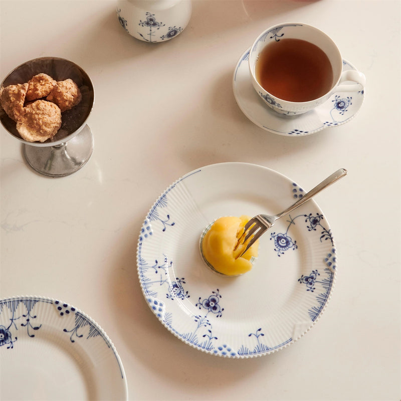 Royal Copenhagen | Blue Elements Plate, 19cm, elegantly holds a dome-shaped yellow dessert, with a matching teacup and cookies on a pale countertop.