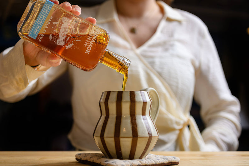 Runamok - Salted Caramel Infused Maple Syrup 250ml being poured into a striped mug, showcasing its use in enhancing beverages and breakfast dishes.