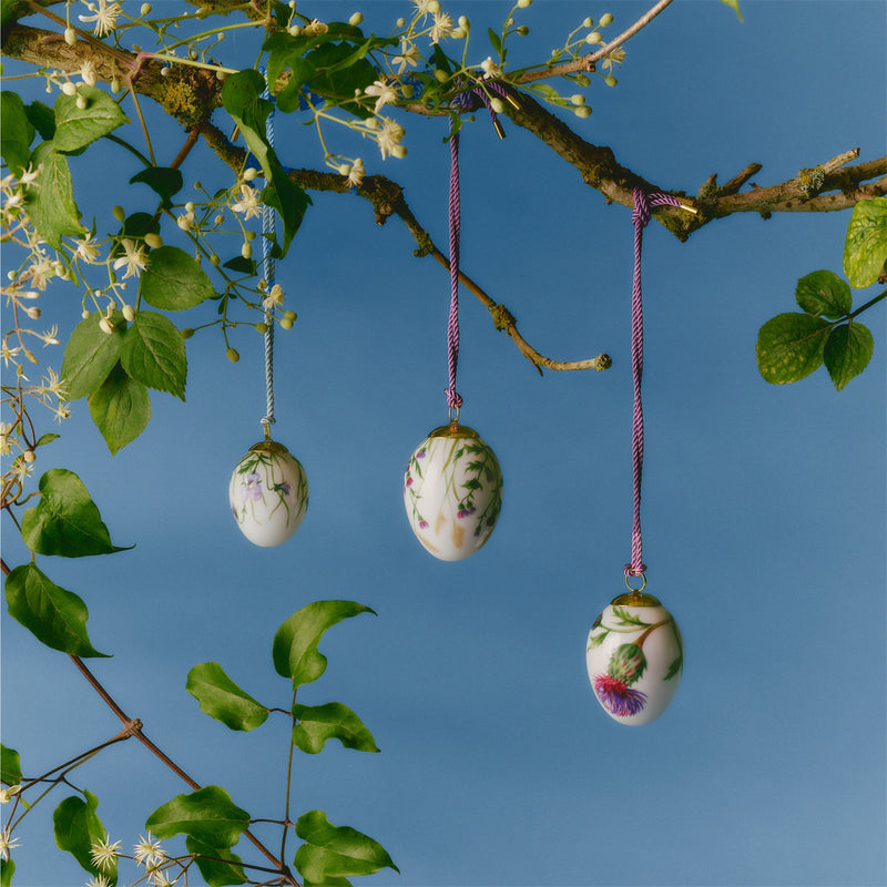 Royal Copenhagen Spring 2026 Eggs Thistle 6cm 2pc features porcelain egg ornaments with intricate floral designs, suspended among white blossoms, embodying elegant Danish spring motifs.