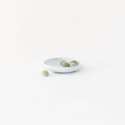 Sarah Kersten - Olive Dish: Basin Collection: Fig, featuring green olives on a small white plate, ideal for appetizers. Perfect for kitchen enthusiasts seeking versatile serving pieces.