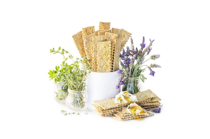 Rustic Bakery - Flatbreads - Herbs de Provence Organic Sourdough crackers with soft cheese and honey, surrounded by fresh herbs and lavender blossoms.
