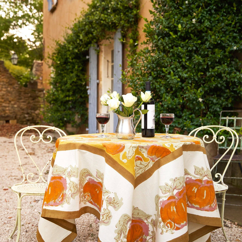 Caravan Home - Pumpkin Orange & Mustard Tablecloth: A vibrant table setting with a handprinted linen featuring abstract pumpkins, perfect for autumn gatherings, on a patio with wine and roses.